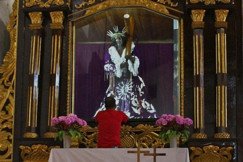 A person in a red shirt performing a religious ceremony in front of a large, ornate religious icon. 5