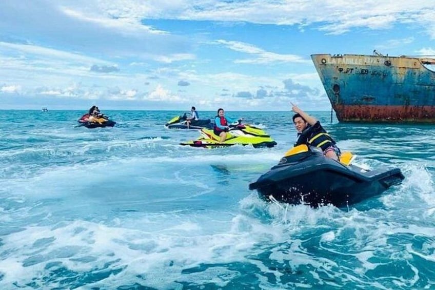 Personer som åker vattenskoter på havet med ett stort, rostigt fartyg i bakgrunden. 5