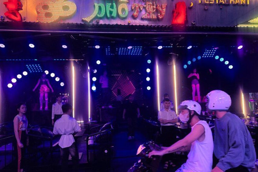 A DJ booth with a crowd, a stage with performers, and a neon sign. 2