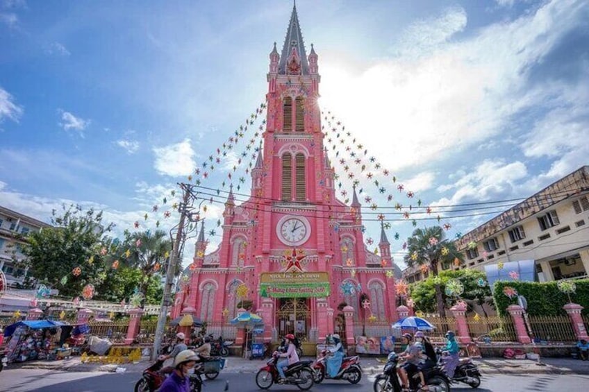 A pink church with a clock tower, surrounded by a street with motorbikes and pedestrians. 5