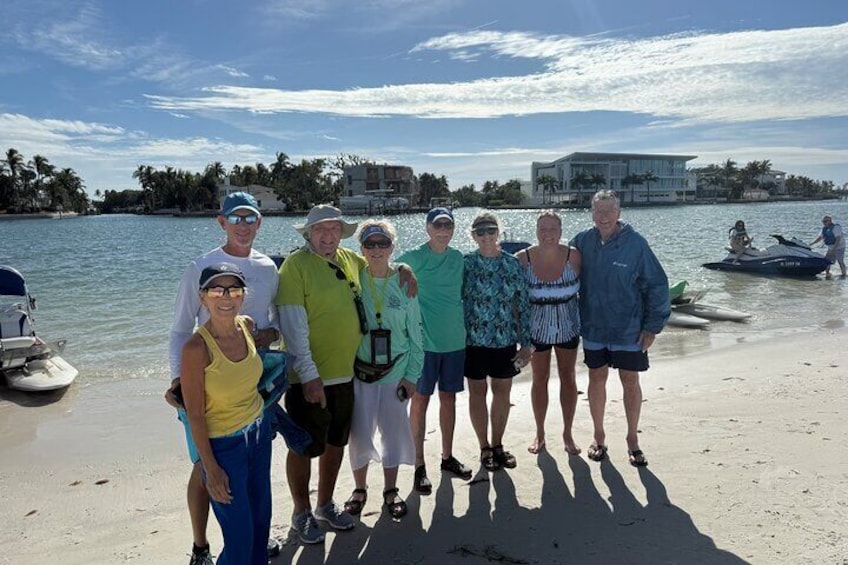 En grupp människor som står på en strand, med en båt och en vattenskoter i bakgrunden. 4
