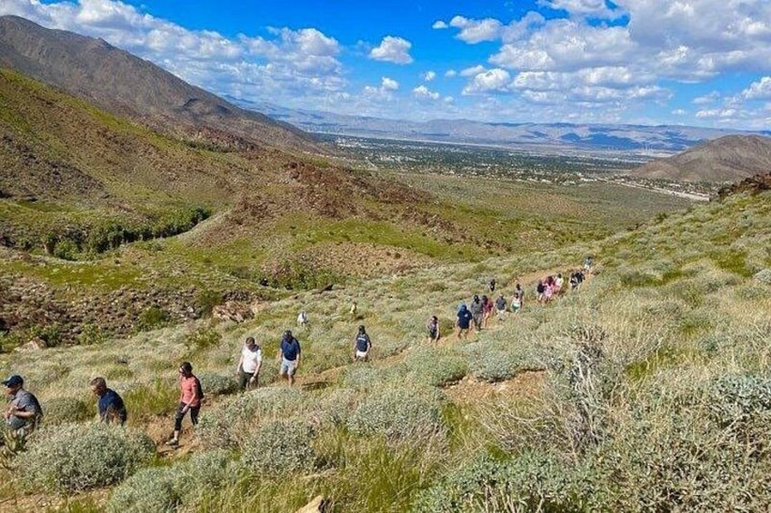 A group of hikers on a trail in a mountainous area with sparse vegetation and distant cityscape. 2