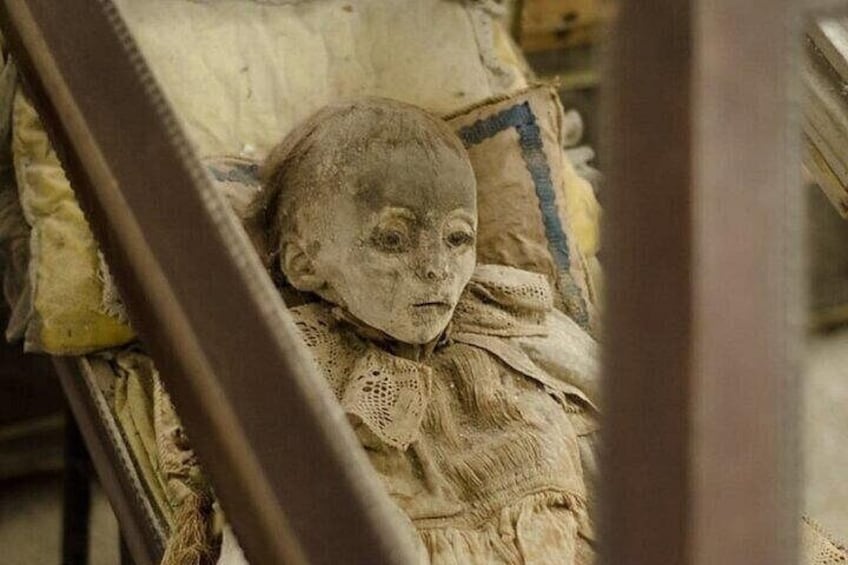 A doll with a ruffled collar lying on a bed with a patterned blanket. 3