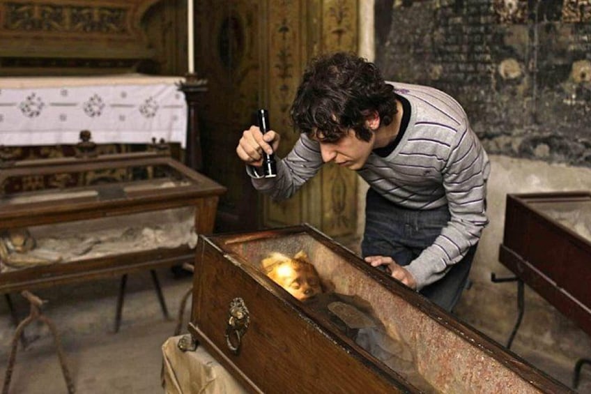 A person examining a wooden chest in a room with religious artifacts. 2