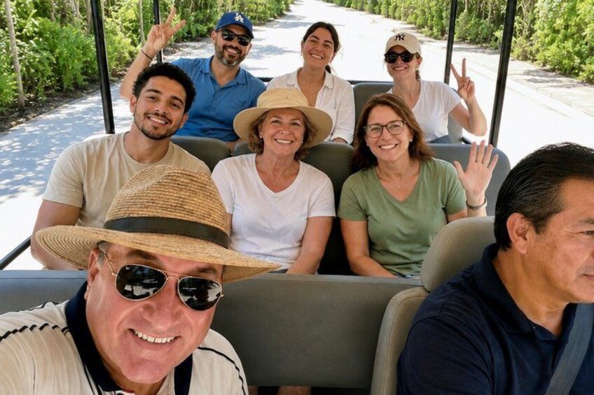 Un gruppo di persone su un veicolo, forse un golf cart, con vegetazione e un sentiero sullo sfondo. 5