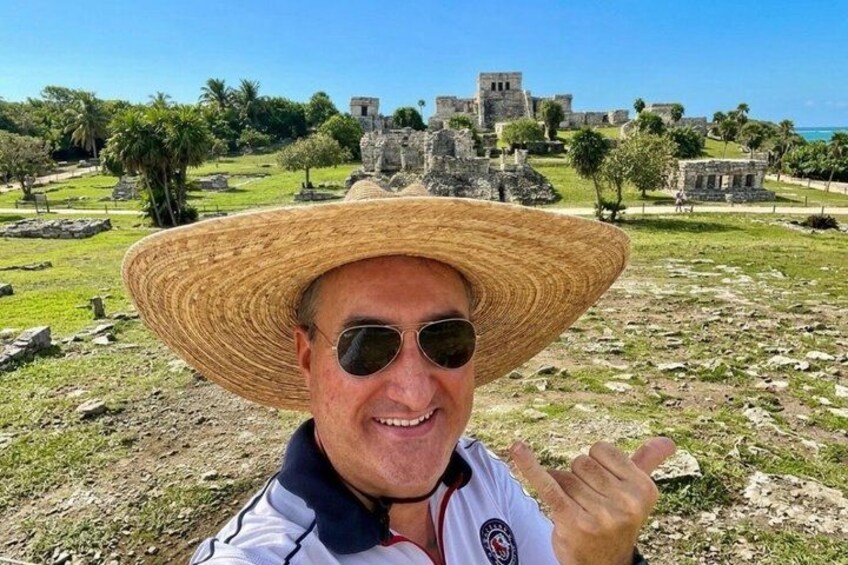 Una persona con un cappello di paglia e una maglia sportiva, in piedi di fronte a rovine antiche sotto un cielo sereno. 4
