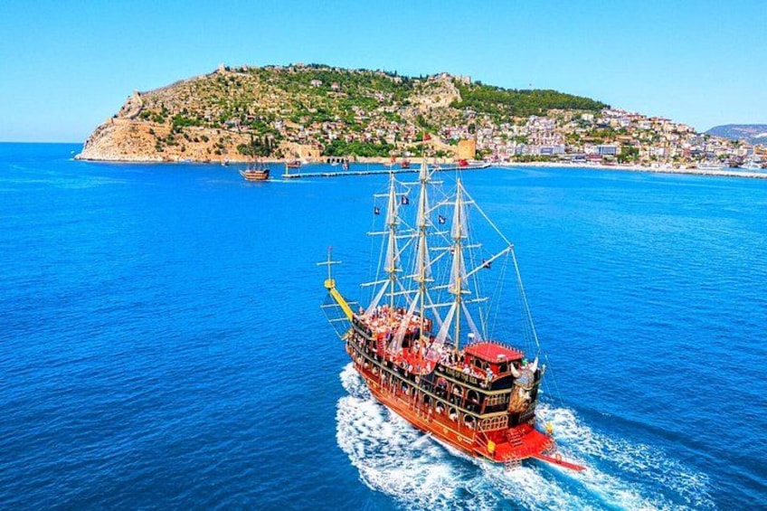 A red sailing ship on a blue sea with a hilly island in the background. 1