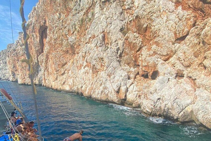 A rocky coastline with clear blue water, a boat with people on board, and a person swimming in the water. 3