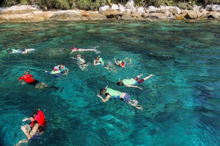 People swimming in clear water with rocks in the background. 2