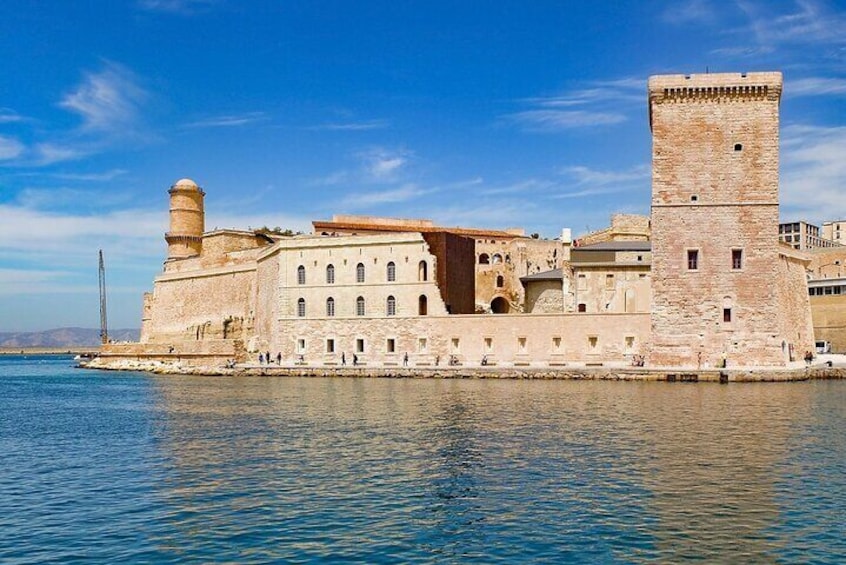 A historic stone fortress by the sea with a prominent tower and a large building with arched windows. 1
