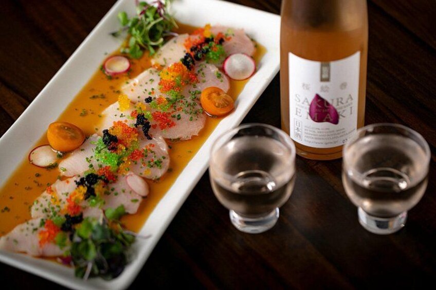 Een schotel sashimi met roe en garnering, vergezeld van een fles sake en twee shotglazen. 4