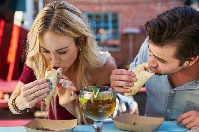 Twee personen eten aan een buitentafel, met een drankje ervoor. 1