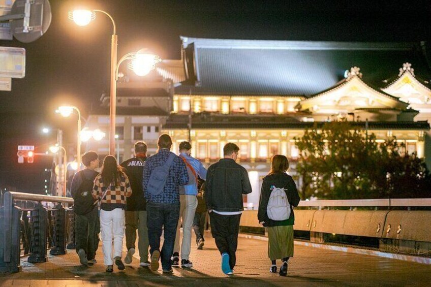 A group of people walking on a bridge at night with illuminated buildings in the background. 3