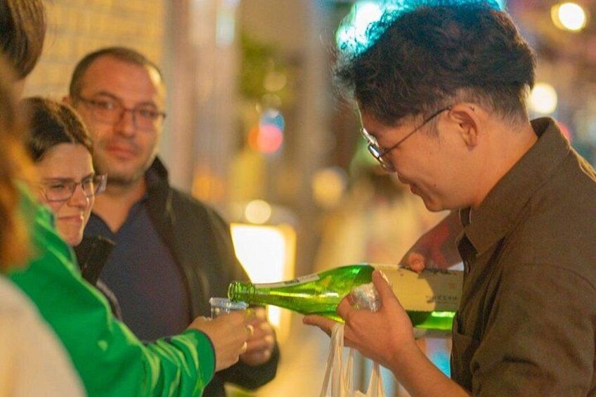 En person hælder drik fra en grøn flaske i et glas. 2