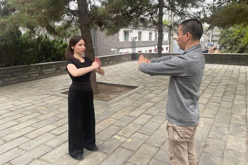 Two people practicing Tai Chi in an outdoor setting with trees and a paved area. 4