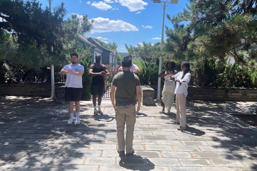A group of people standing on a stone pathway in a park with trees and a building in the background. 2