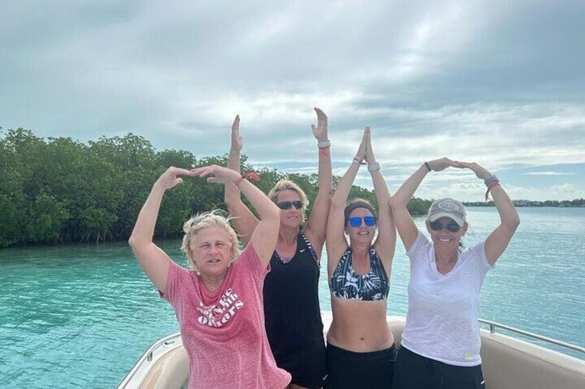Four people on a boat with their arms raised, surrounded by water and greenery. 4
