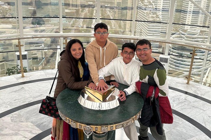 A group of people posing around a table with a cake in a modern building with large windows. 3