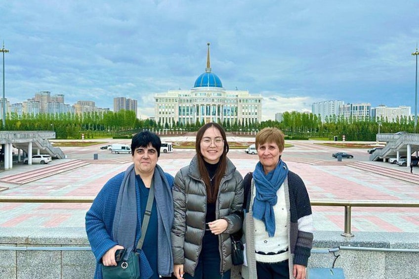 Three people standing in front of a large building with a blue dome, a paved area, and modern buildings in the background. 4