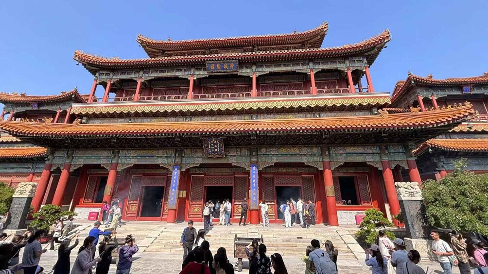 A traditional multi-tiered building with ornate red and green roofs, surrounded by visitors. 1