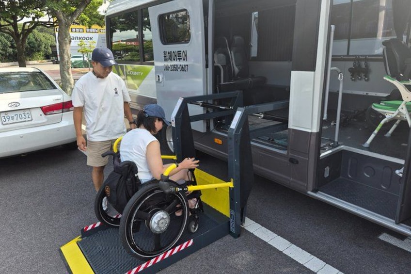 Una rampa para silla de ruedas que conduce a un autobús, una persona en silla de ruedas y un coche aparcado cerca. 1