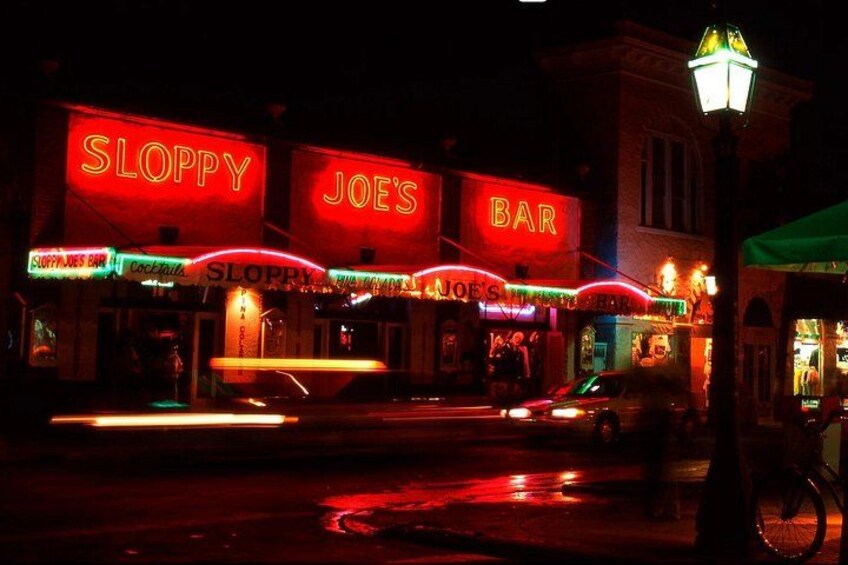 Un bar chiamato Sloppy Joe's con insegne al neon, una strada con veicoli e un lampione. 1