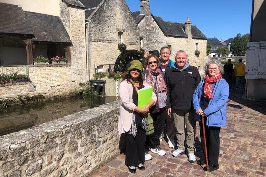 A group of people standing in front of a stone building with a water wheel. 4