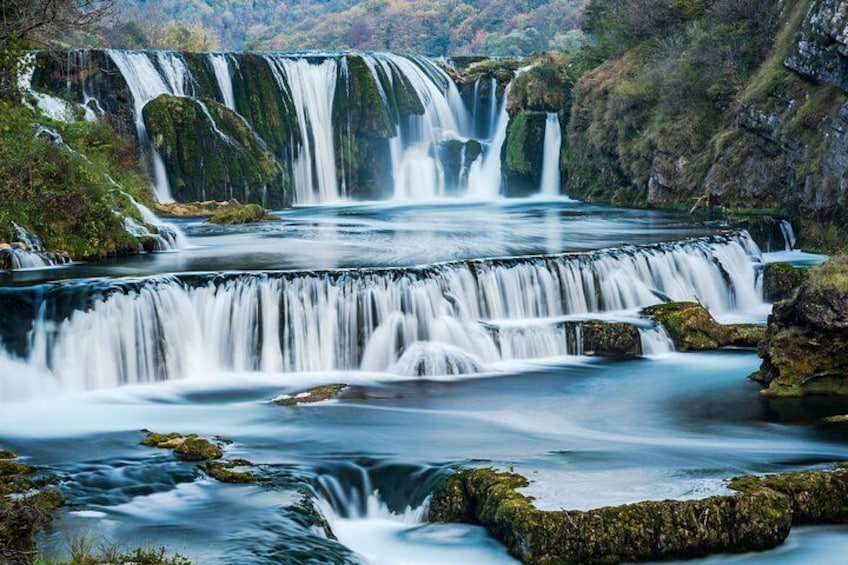Een meerlaagse waterval met stromend water over rotsen en een mosgroen landschap. 1