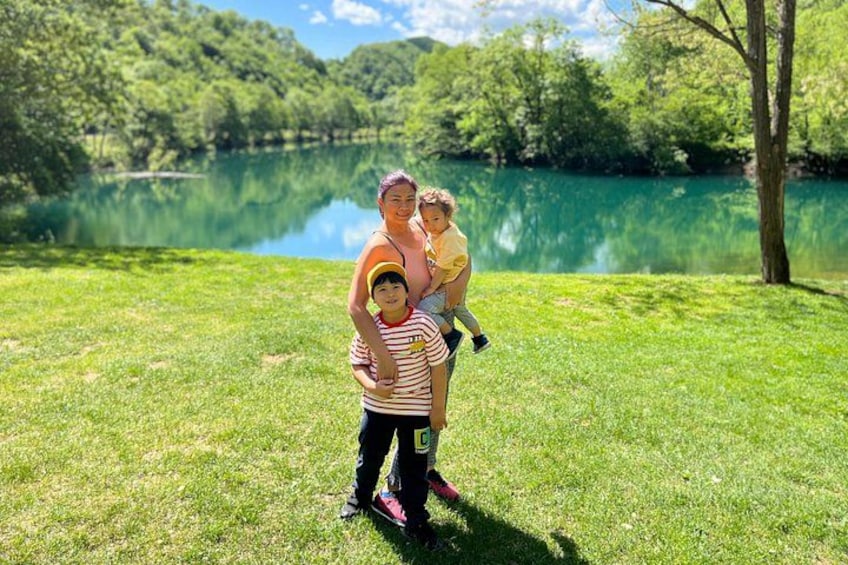 A woman holding a child by a lake with trees in the background. 4