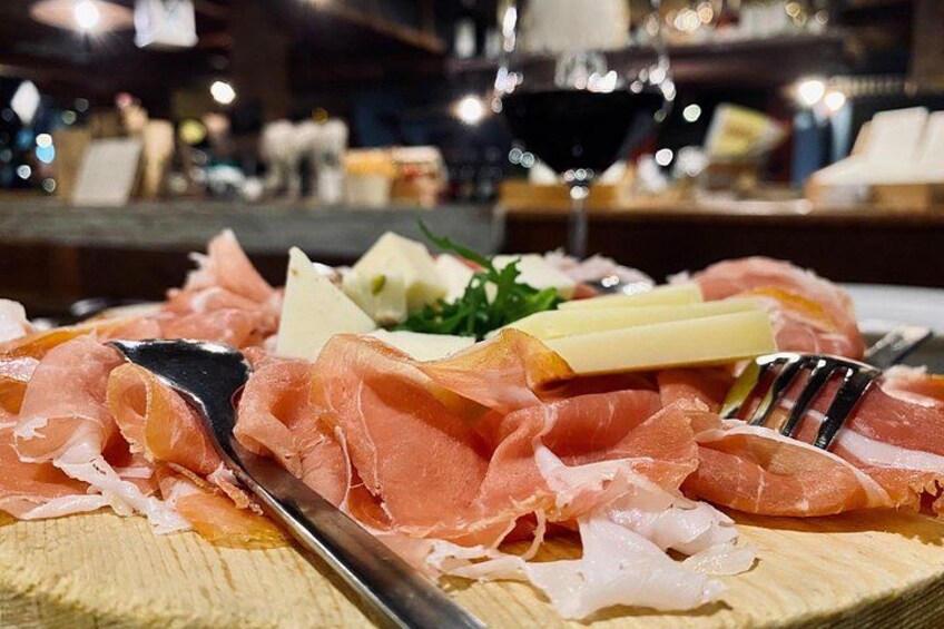 A platter of thinly sliced cured meats, cheese, and a fork on a wooden board. 2