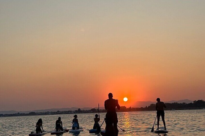 People paddleboarding on a calm body of water during sunset. 1