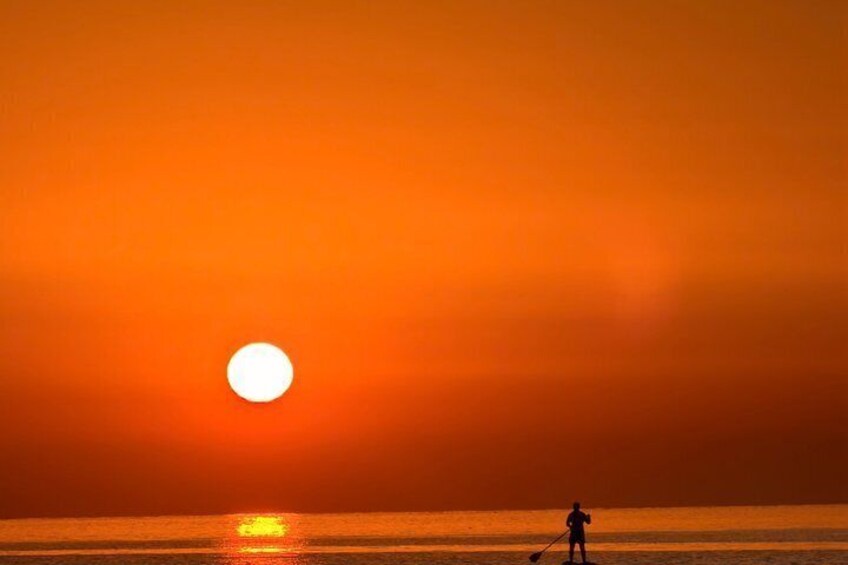 A sunset over the ocean with a silhouette of a person paddleboarding. 4