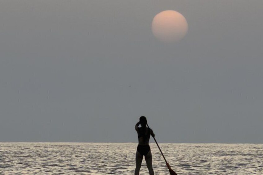 A person paddleboarding on calm water during sunset. 2