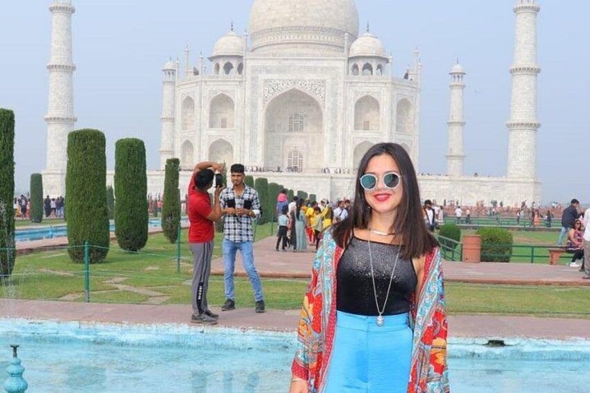 A person standing in front of the Taj Mahal with a pool and manicured bushes in the background. 5