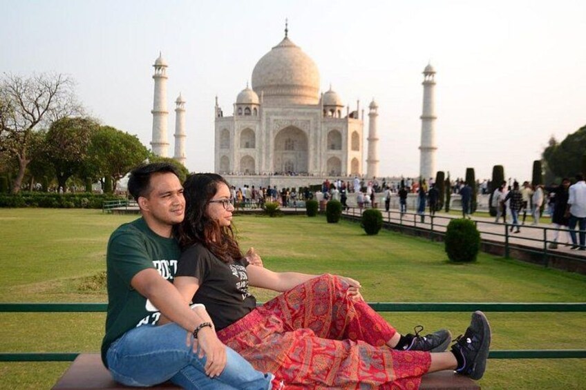 A couple sitting on a bench with the Taj Mahal in the background. 3