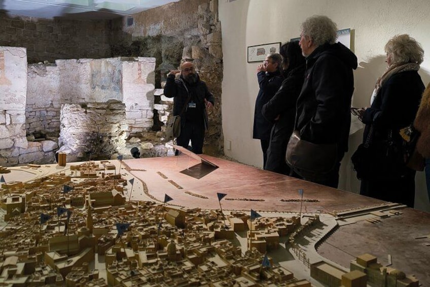 A model of an ancient city with ruins and a group of people observing it. 2