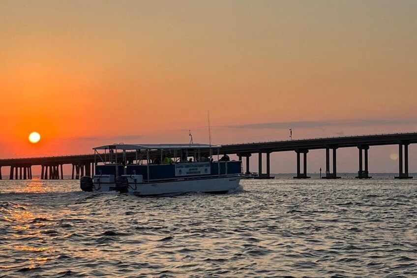 A boat on a body of water with a bridge in the background during sunset. 3