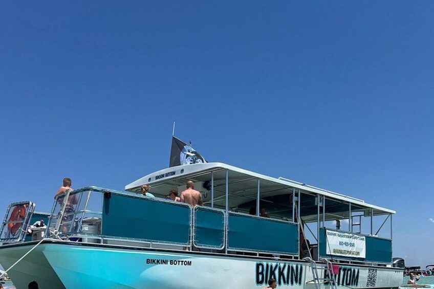 A boat named 'Bikkini Bottom' with people on board, a clear blue sky, and a flag. 2