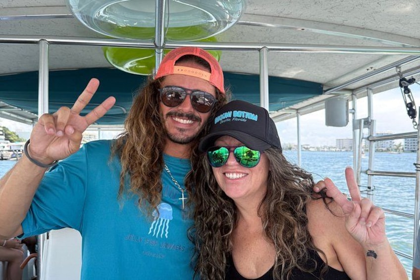 Two people on a boat, one wearing a blue shirt and the other a black top, both making peace signs. 4