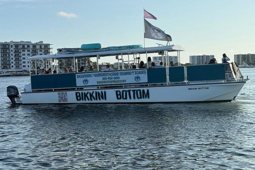 A boat named 'Bikkini Bottom' with a flag, passengers, and a cityscape in the background. 3
