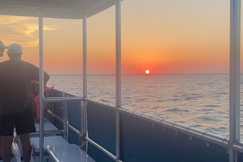 A sunset over the ocean, a boat with metal railings, and two people on the deck. 2