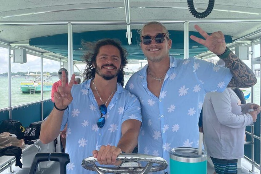 Two people on a boat, one holding a steering wheel, and another making a peace sign. 2