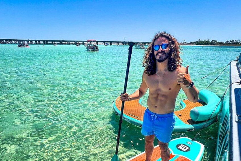 A person paddleboarding on clear turquoise water with a pier in the background. 4
