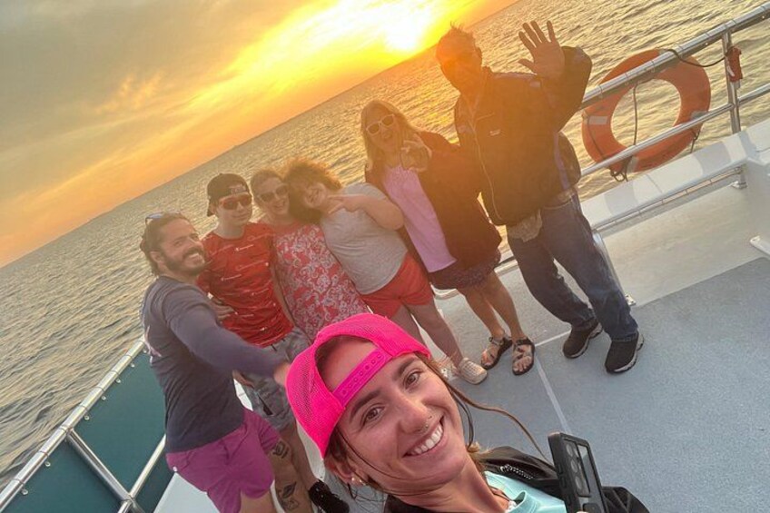 A group of people on a boat with the sun setting in the background. 2