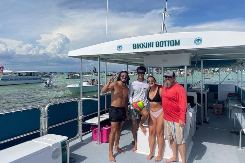 Un bote llamado BIKKIN BOTTOM con gente en la cubierta, agua al fondo y otros botes a la vista. 4