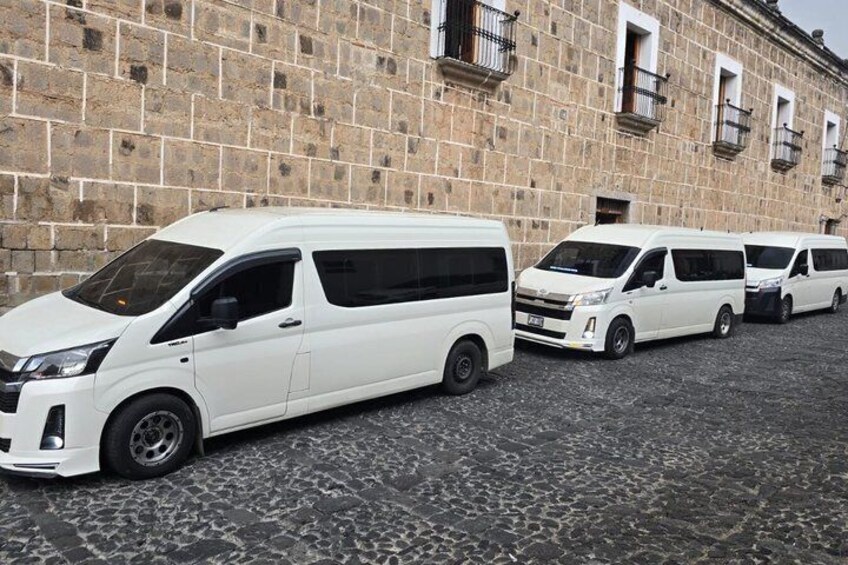 A row of white vans parked in front of a stone building with a cobblestone ground. 2