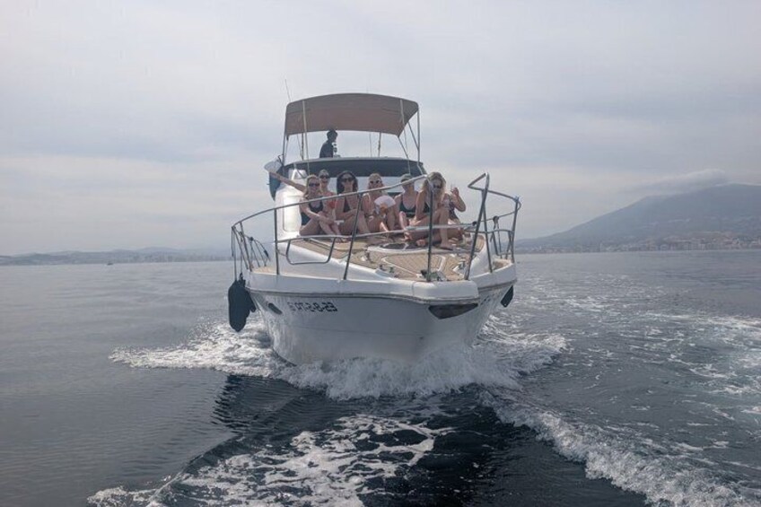 Un bateau blanc avec des personnes à bord, naviguant sur une eau calme, avec une vue sur la ville et des montagnes en arrière-plan. 3