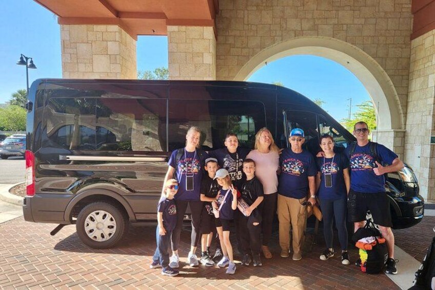 A group of people posing in front of a black van under a stone archway. 5