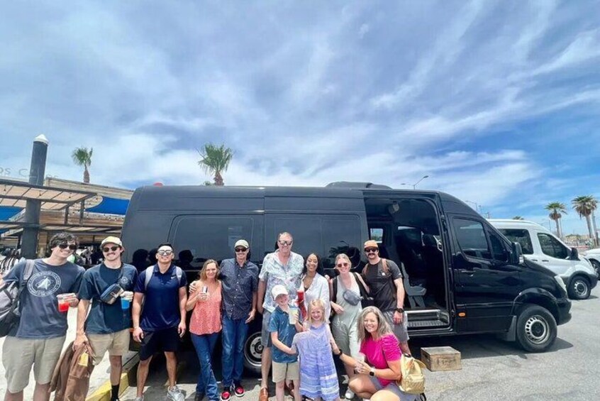 A group of people standing in front of a black van with palm trees and a building in the background. 2