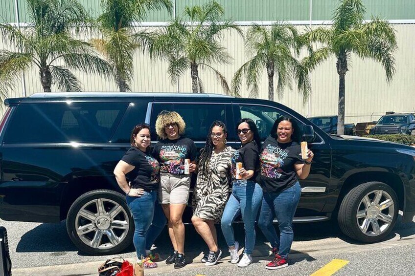 A group of people posing in front of a black SUV with palm trees in the background. 1